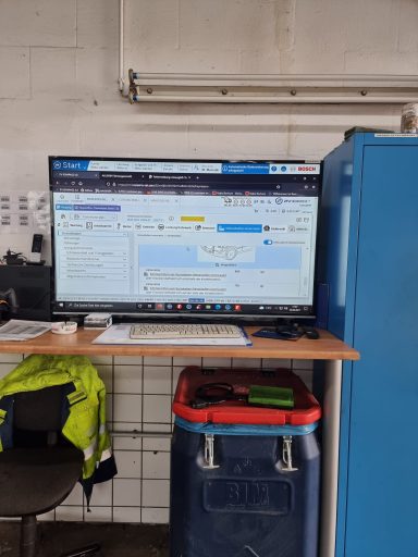 Ein großer Monitor zeigt eine Webseite, daneben ein Müllbehälter und eine Arbeitsfläche.